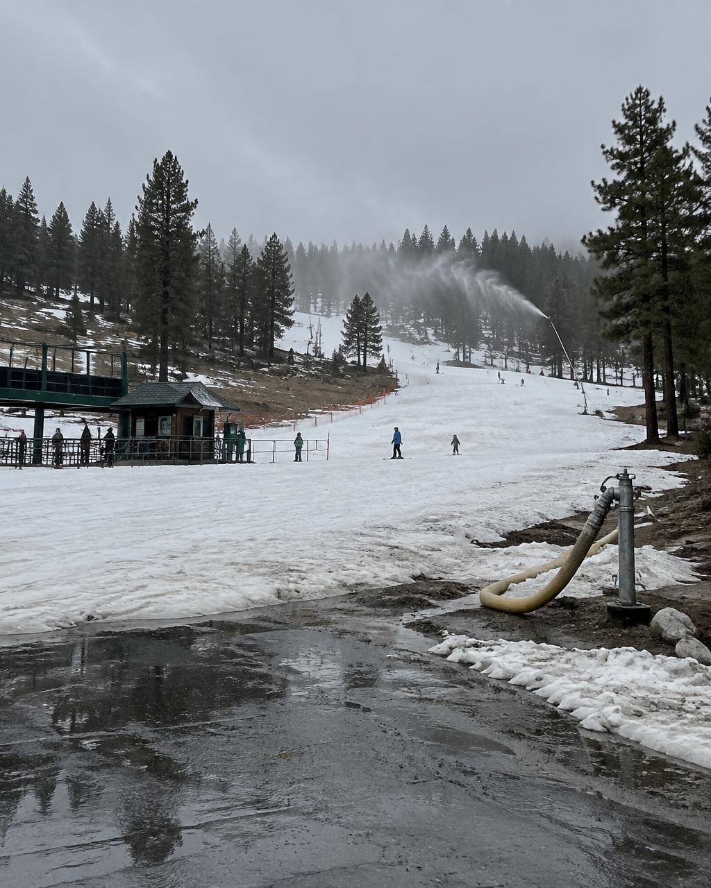 Wet shoulder-season snow at the lower base area, with a snowmaking hydrant and bare patches