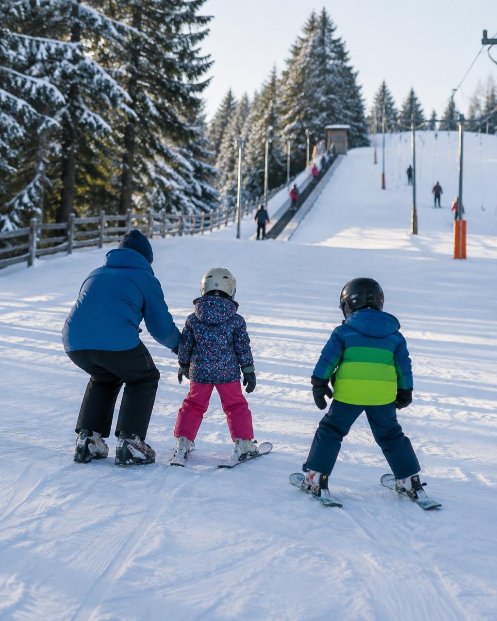 An instructor teaching two small children to ski on a gentle beginner slope beside a magic carpet