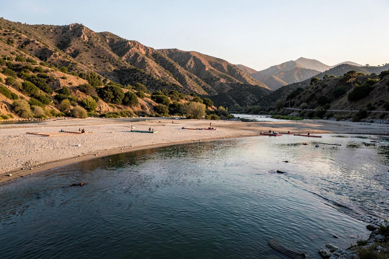 A calm pool and sandy beach on a wide foothill river with rafts drawn up in the evening light