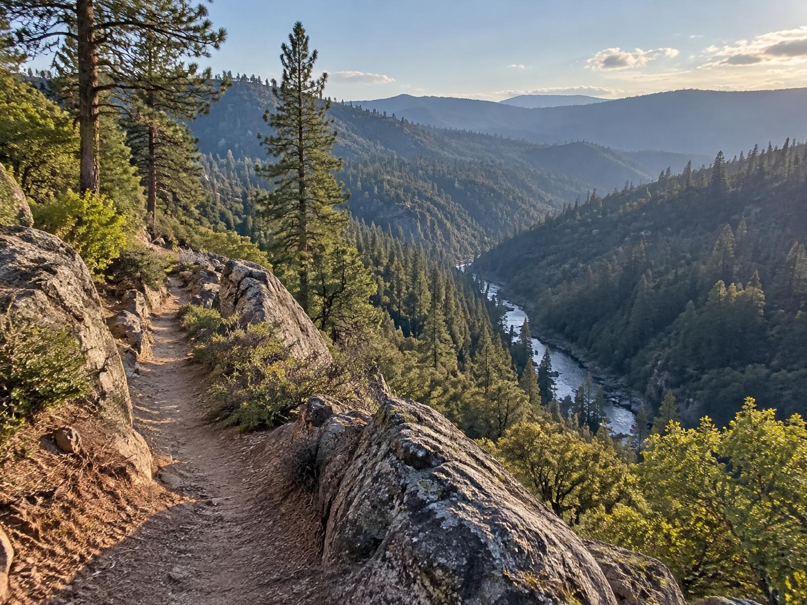 A rocky singletrack overlook on the Arnold Rim Trail above the forested river canyon