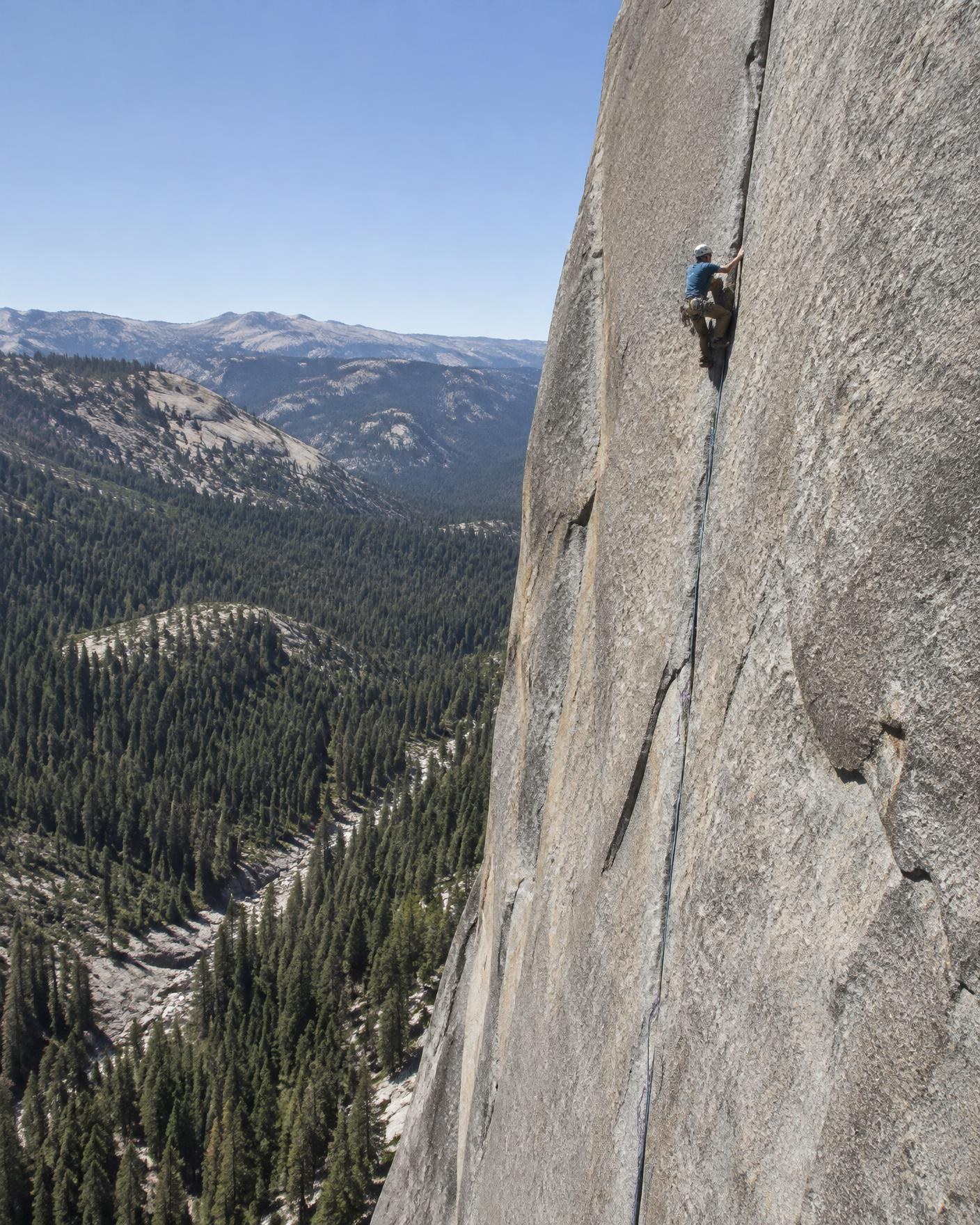 A climber leading a long crack on the granite face of Calaveras Dome above a forested canyon