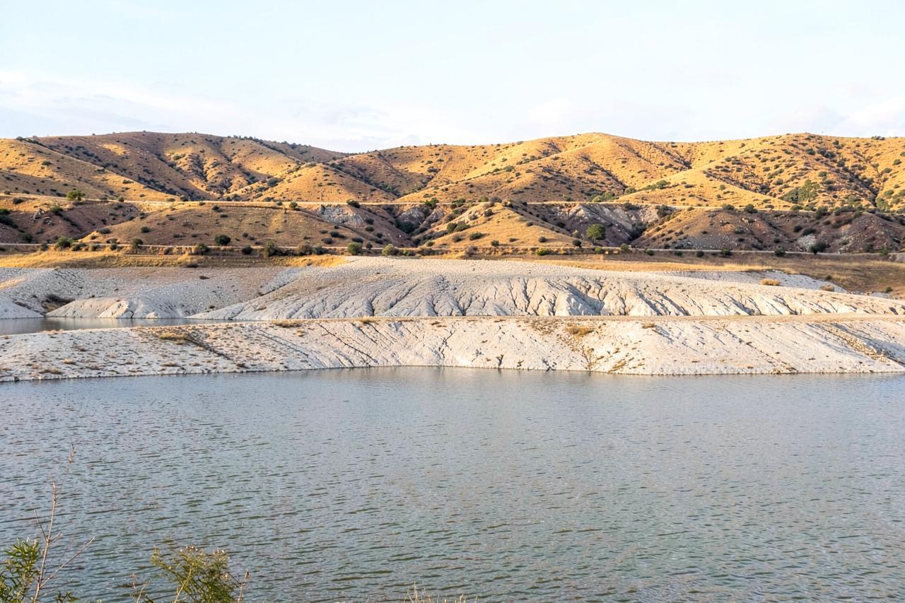A reservoir at low water showing a wide pale band of bare exposed rock below the golden hills