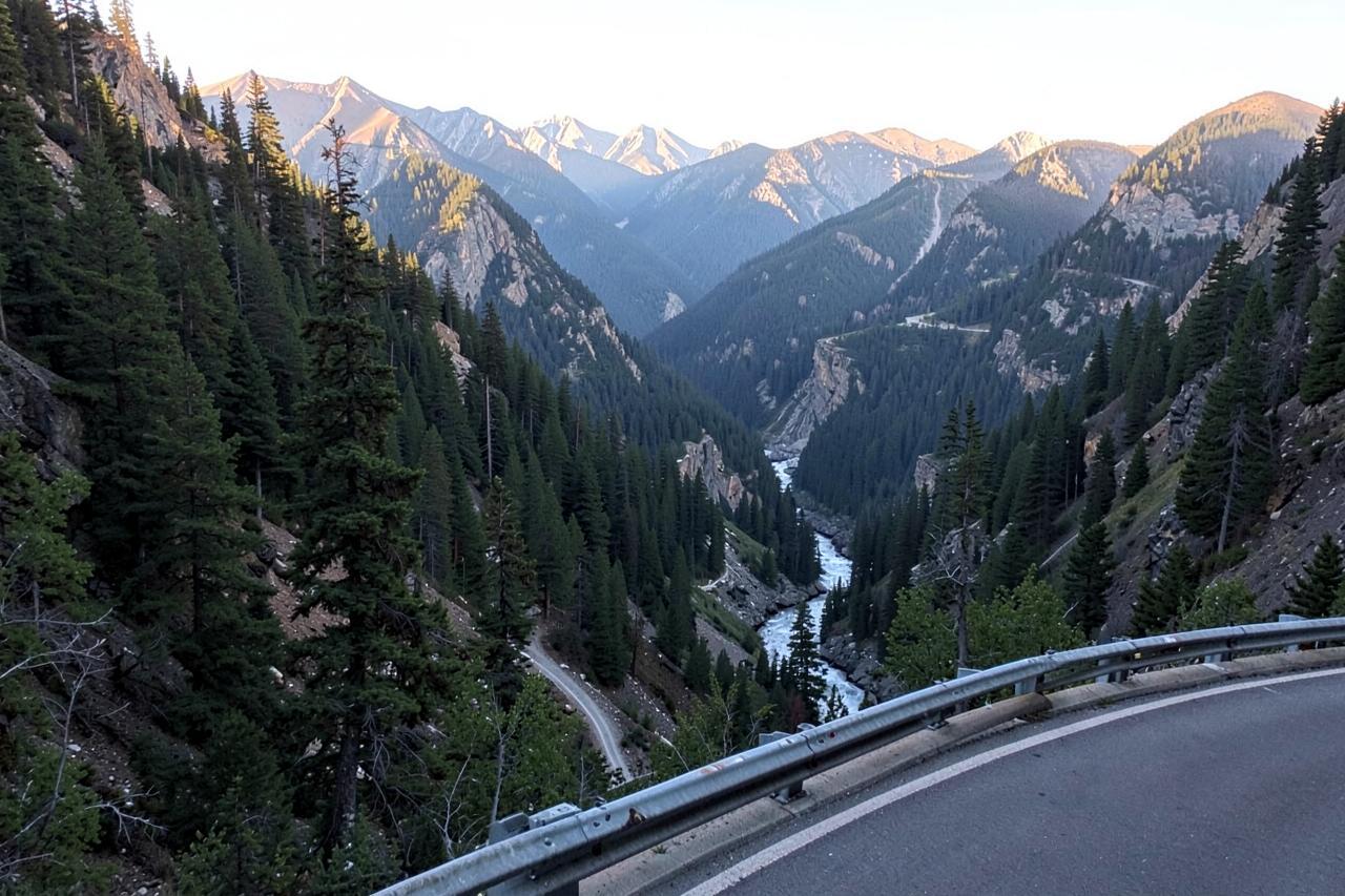 A two-lane highway curving along a forested ridge high above a deep river canyon at dusk