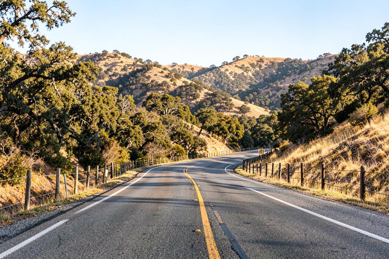 A two-lane highway curving between golden oak-covered foothills