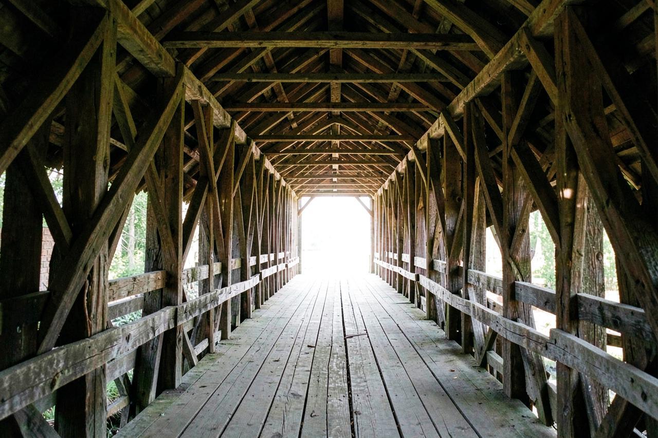The timber trusses and plank deck inside an old covered bridge, lit by the far opening