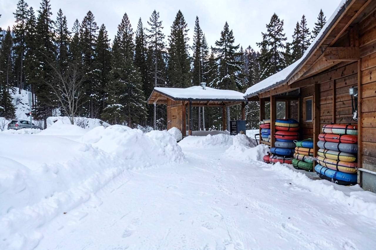 A snowy base area with a timber warming hut and stacks of coloured snow tubes beside plowed banks