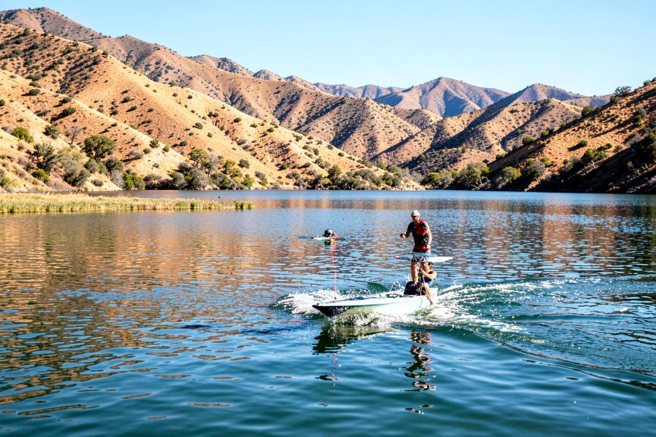 A small motorboat towing a rider across calm reservoir water between bare golden hills